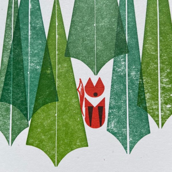 An image of a letterpress printed card. The card is printed with simple geometric shapes in a design featuring a group of pine trees in different shades of green, and a red fox sitting among the trees.