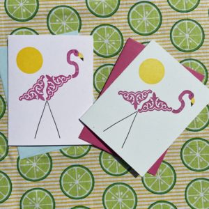An image of two letterpress cards. Both feature a plastic lawn flamingo render in letterpress type ornaments. The flamingo is pink with black legs and a yellow beak.